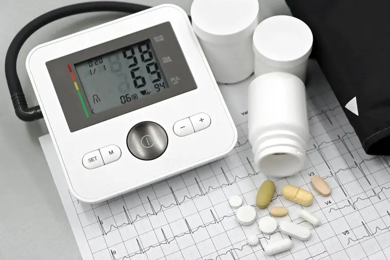 Blood pressure monitor with pills on ECG sheet, essential for heart health management.